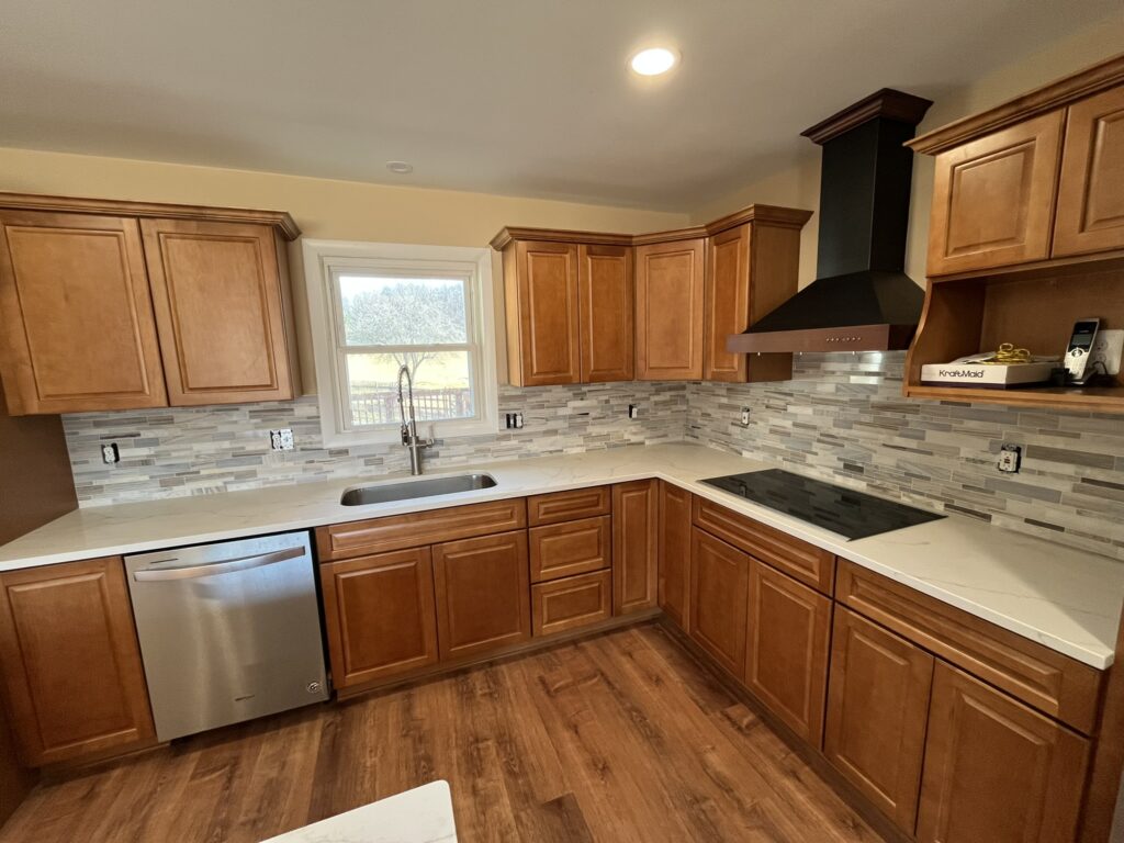 Warm Wood Kitchen Remodel with Modern Finishes Modern kitchen remodel with warm wood cabinets, white countertops, tile backsplash, and black range hood