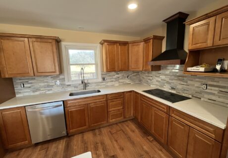 Modern kitchen remodel with warm wood cabinets, white countertops, tile backsplash, and black range hood