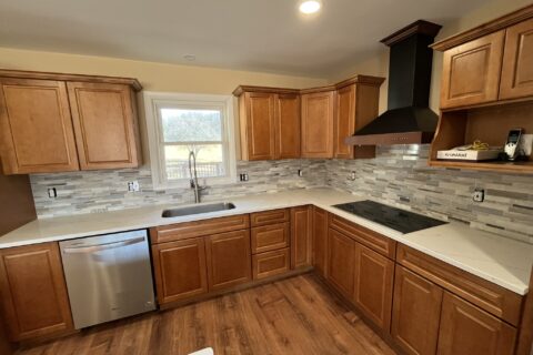 Modern kitchen remodel with warm wood cabinets, white countertops, tile backsplash, and black range hood