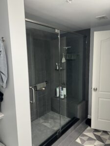 Walk-in glass shower with dark tile, built-in bench, grab bar, and corner storage in a remodeled bathroom
