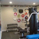 Home gym with weightlifting equipment and decorative wall plates in a remodeled basement.