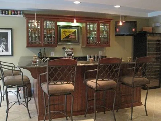 Basement bar with glass-front cabinetry, pendant lighting, and high-back barstools.