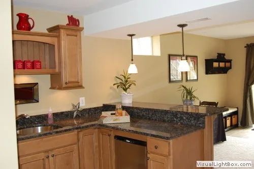 Basement kitchenette with wooden cabinets and granite countertops in a well-lit design.