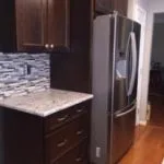 Stainless steel refrigerator surrounded by custom dark cabinetry and granite countertop.