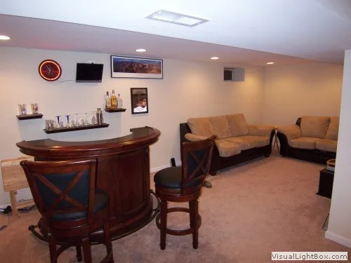 Basement bar and lounge area with curved wooden bar, stools, and cozy seating.
