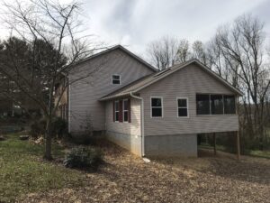 A house with trees in the background and a building on the ground.