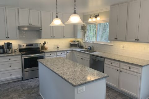 A modern kitchen featuring white cabinets, black countertops, and a stainless steel refrigerator, with pendant lights hanging over a black island.