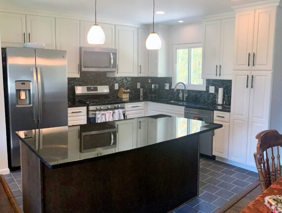 A kitchen with white cabinets and black counter tops.