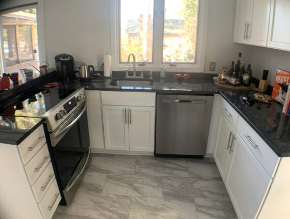 A kitchen with white cabinets and black counter tops.