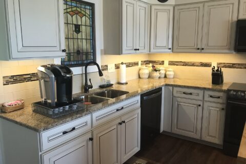 A kitchen with white cabinets and brown wood floors.