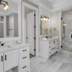Bright remodeled bathroom with double vanity, marble-style surfaces, and walk-in glass shower