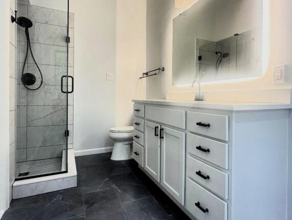 Modern bathroom remodeling project in Columbia MD with walk-in shower, white vanity, and dark tile flooring