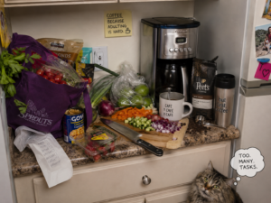 A small kitchen remodeling in Columbia MD with a crowded kitchen countertop with groceries, chopped vegetables, coffee supplies, and a coffee maker all competing for space, while a cat looks up with a thought bubble that says, “Too. Many. Tasks.”