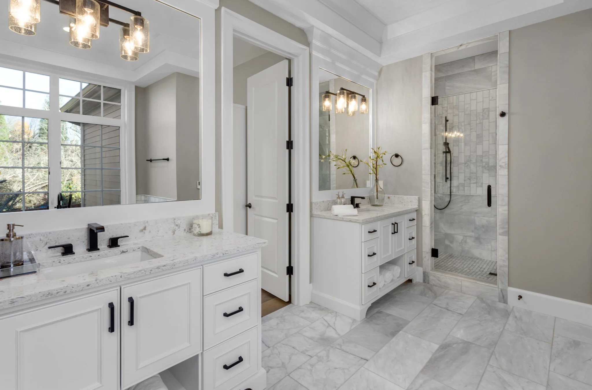 Bright remodeled bathroom with double vanity, marble-style surfaces, and walk-in glass shower