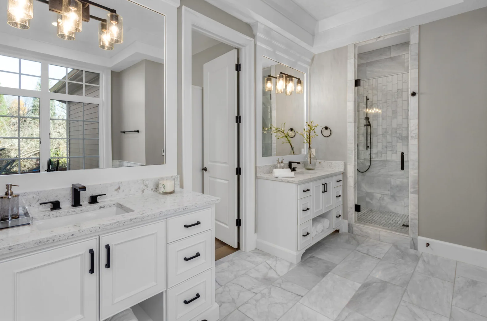 Bright remodeled bathroom with double vanity, marble-style surfaces, and walk-in glass shower